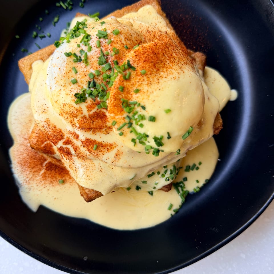 French toast topped with creamy sauce, paprika, and chopped chives on a black plate.