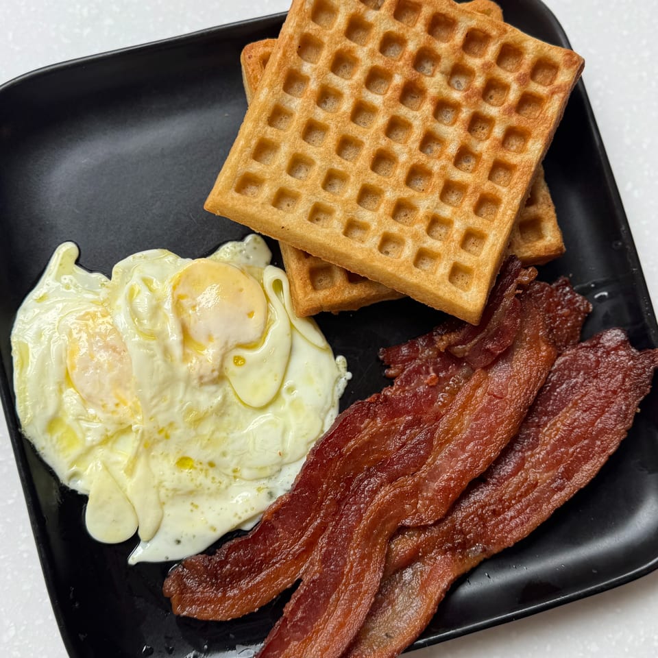 Golden waffles served with fried eggs and crispy bacon on a black plate.